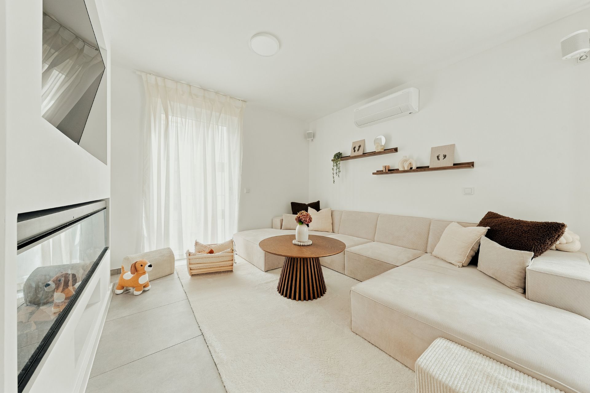 Helles Wohnzimmer mit großer beiger Eckcouch, rundem Holztisch und Spielsachen auf dem Boden.