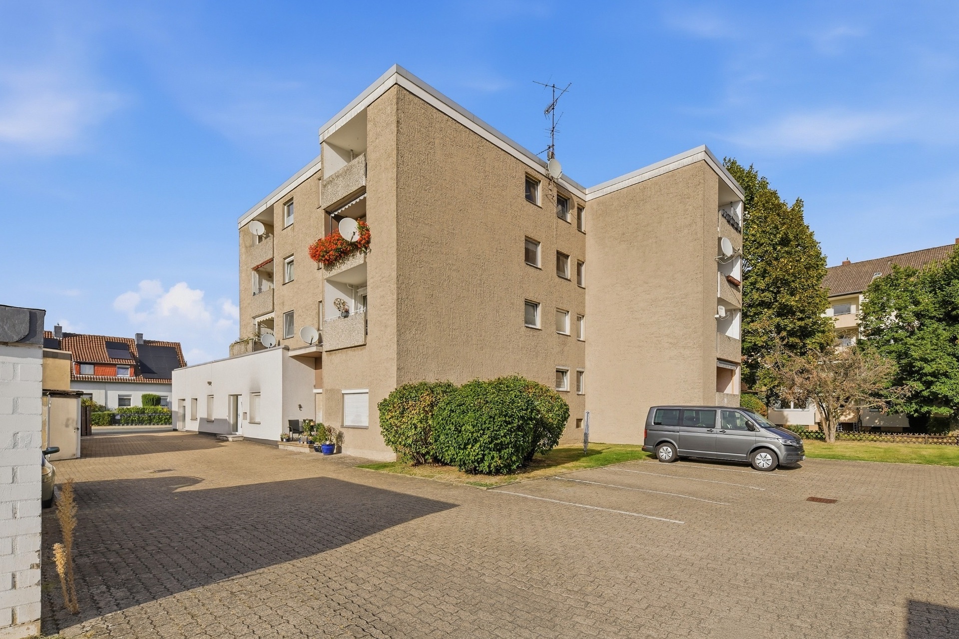 Mehrfamilienhaus mit Balkonen und angrenzendem Parkplatz an einem sonnigen Tag.