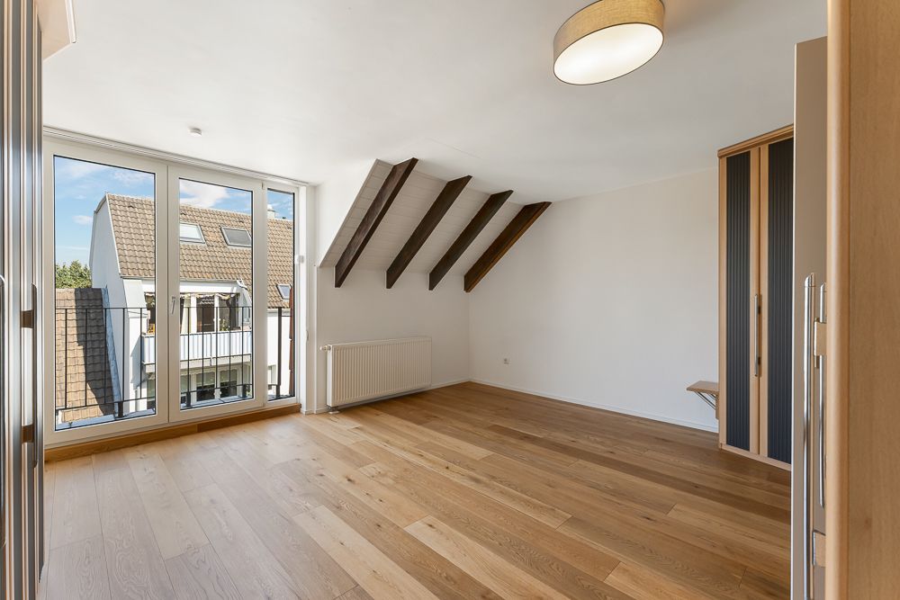 Helles Zimmer mit Holzfußboden, sichtbaren Balken und großen Fenstern zu einem Balkon.