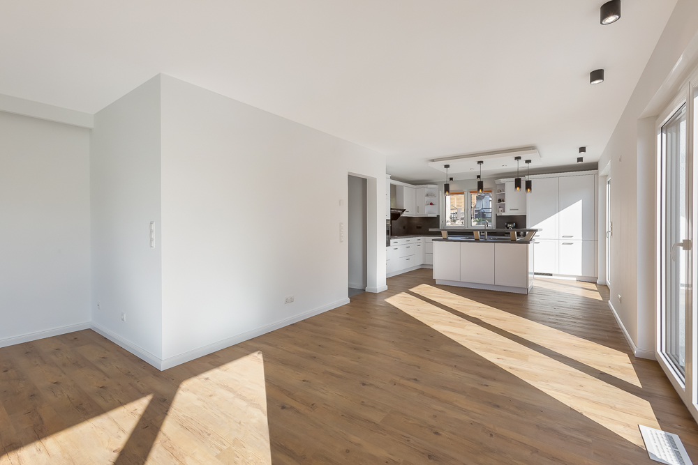 Heller, leerer Wohnraum mit Holzboden und offener moderner Küche.