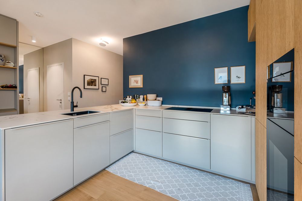 Moderne Küche mit blauen Wänden, weißen Schränken und Einbaugeräten, Teppich auf Holzboden.