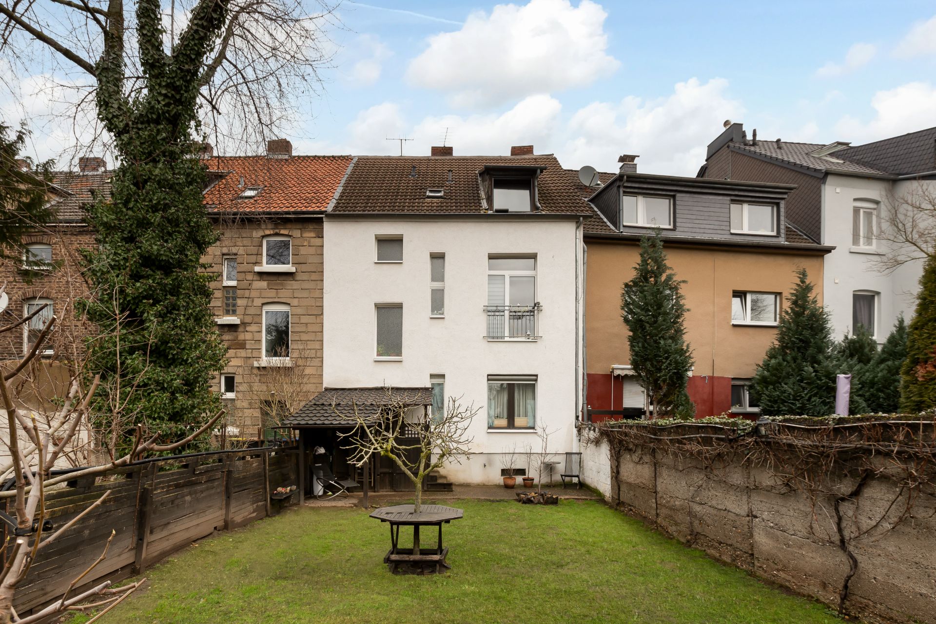 Mehrfamilienhaus mit Garten, Holztisch und Bäumen, umgeben von anderen Wohngebäuden.