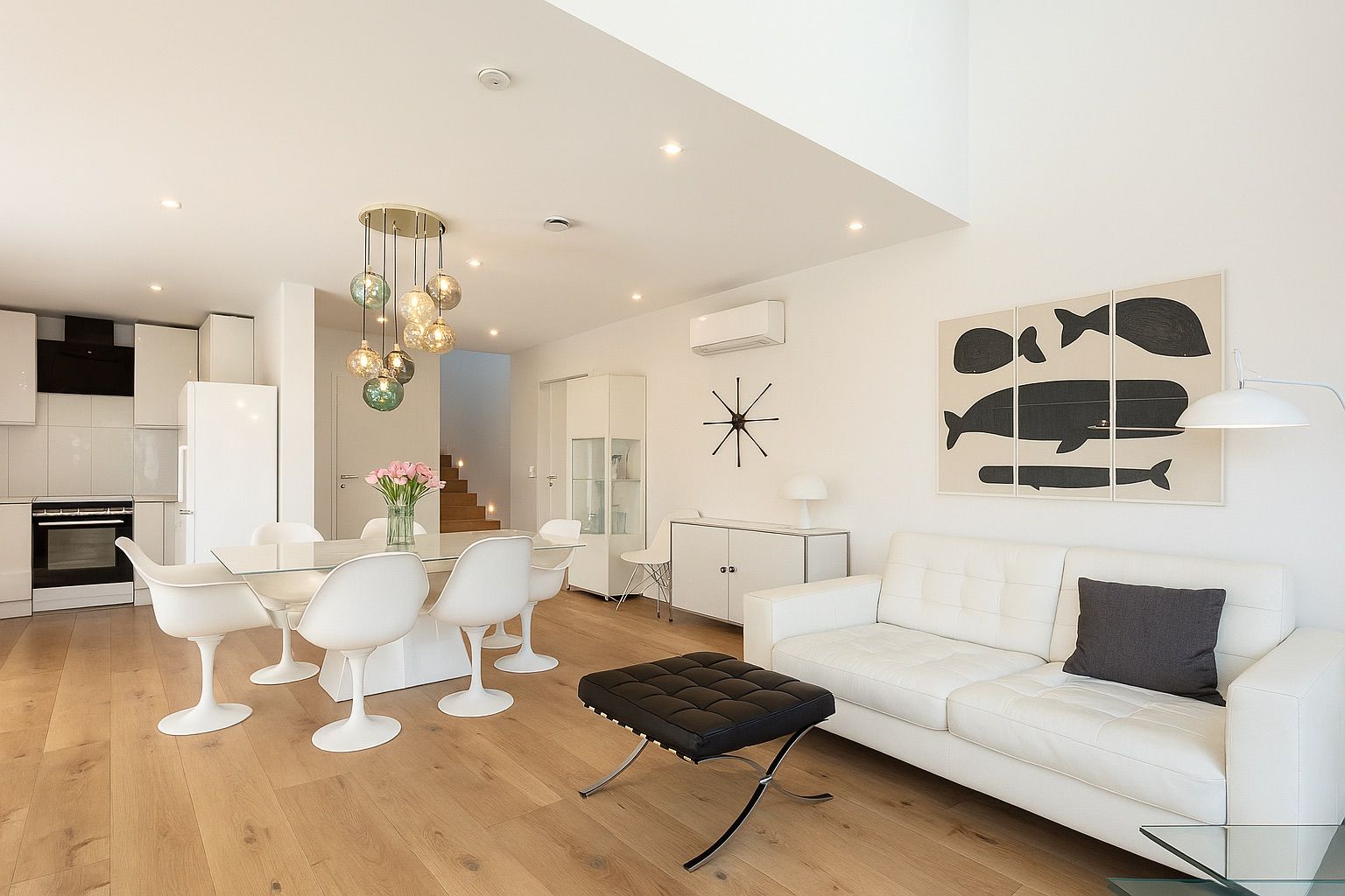 Helles Wohnzimmer mit weißem Sofa, Esstisch, moderner Lampe und Küchenbereich im Hintergrund.