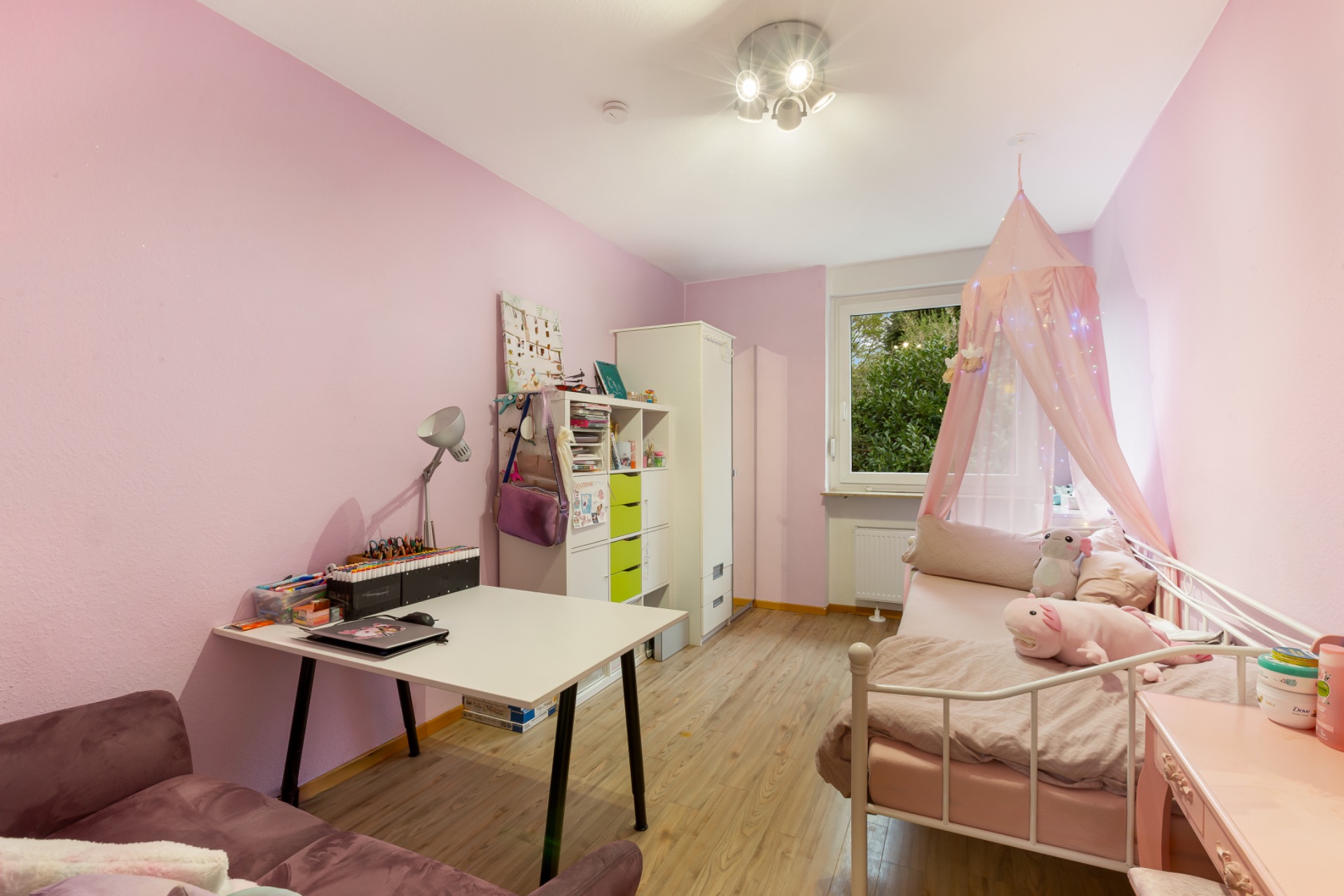 Helles Kinderzimmer mit rosa Wänden, Schreibtisch, Regal und einem Tagesbett mit Baldachin.
