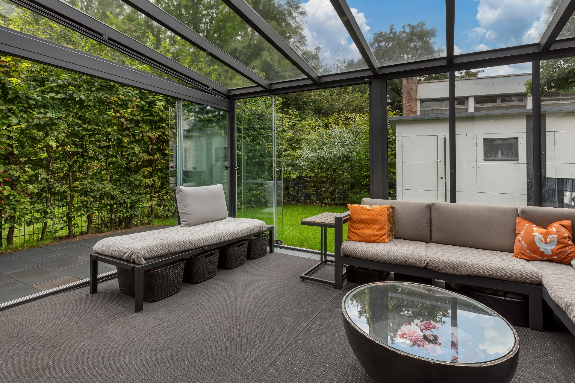 Wintergarten mit Sitzbank, Sofa mit Kissen, Glastisch und Blick auf Garten.