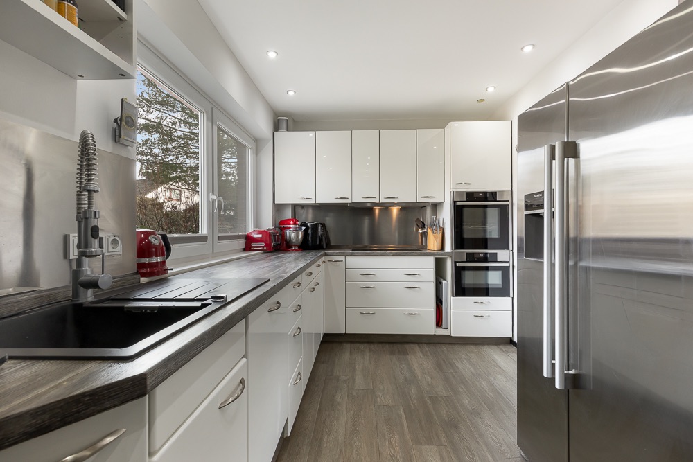 Moderne Küche mit weißen Schränken, großem Kühlschrank und Geräten auf der Arbeitsfläche.
