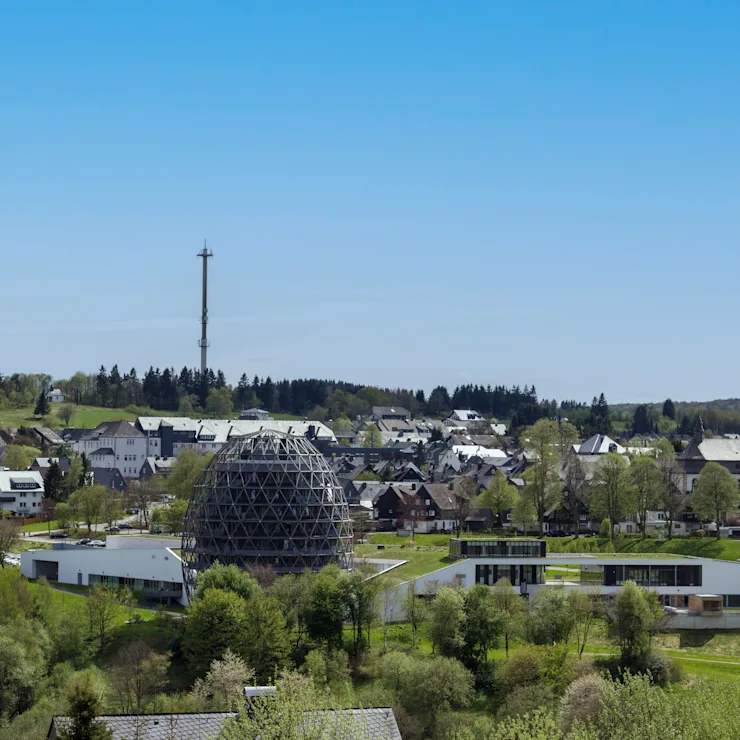 Weitläufige Landschaft mit Hügeln, Feldern, Wald und einem Dorf im Tal unter blauem Himmel.