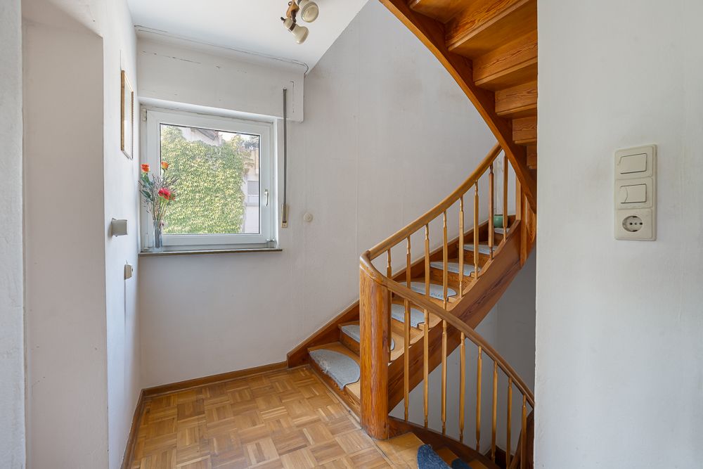 Heller Flur mit Holztreppe und Fenster mit Blick ins Grüne.