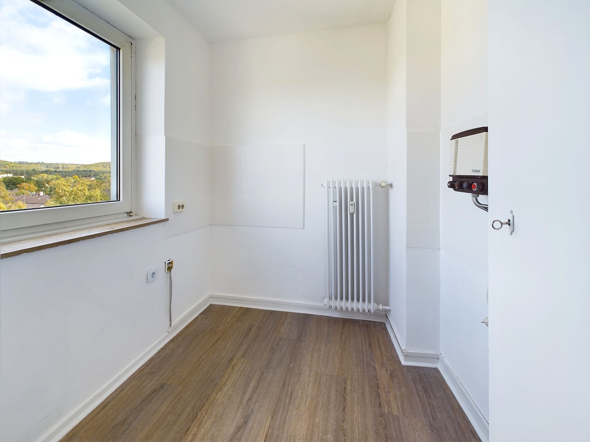 Kleiner leerer Raum mit Fenster, Heizkörper und Holzfußboden.