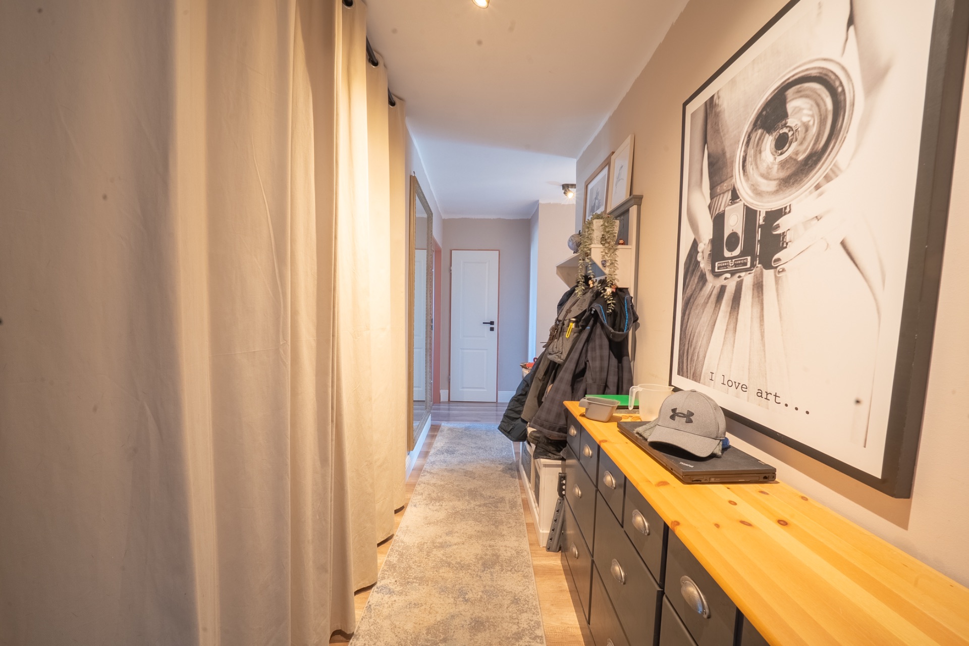 Heller Flur mit Garderobe, Kommode, gerahmtem Bild und Vorhang an der Seite.