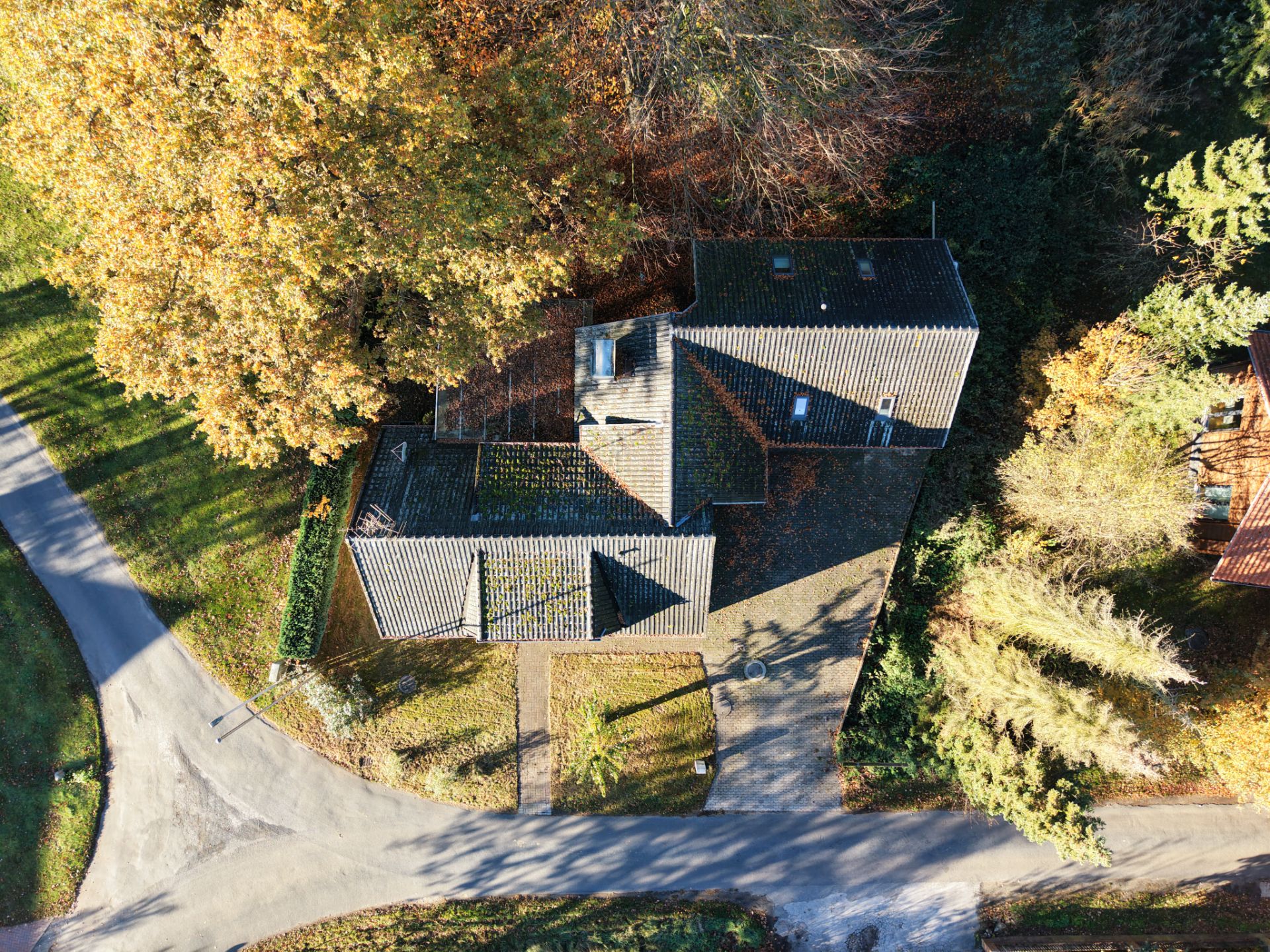 Luftaufnahme eines Hauses mit dunklem Dach an einer Kreuzung, umgeben von Bäumen und Straßen.