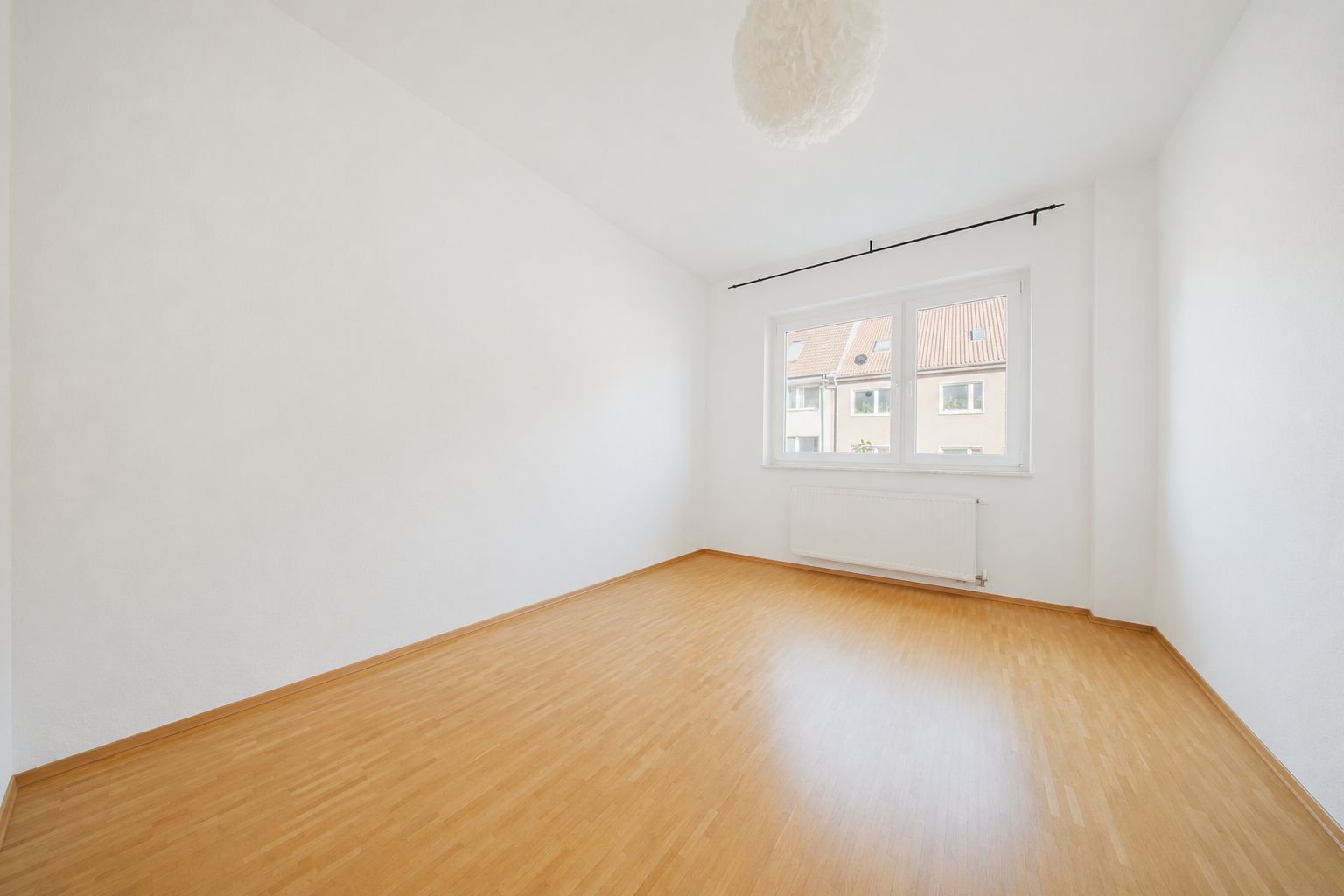 Leerer Raum mit hellem Holzboden, weißen Wänden und großem Fenster.