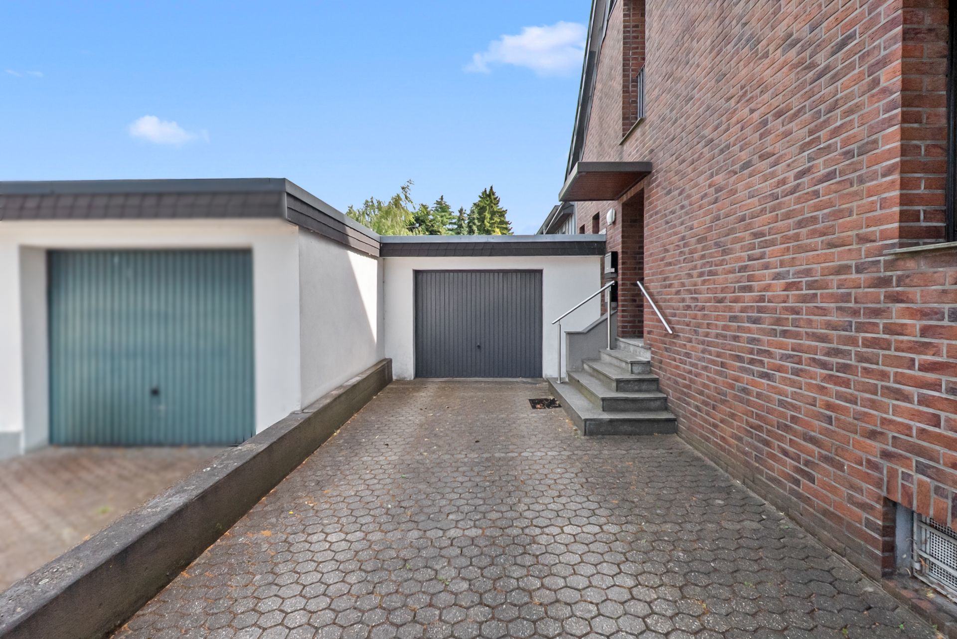 Gepflasterte Einfahrt mit Garage und Treppe an einem Backsteinhaus.