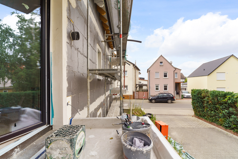 Blick von einem Balkon mit Baugerüst und Baumaterialien auf eine Wohnstraße.