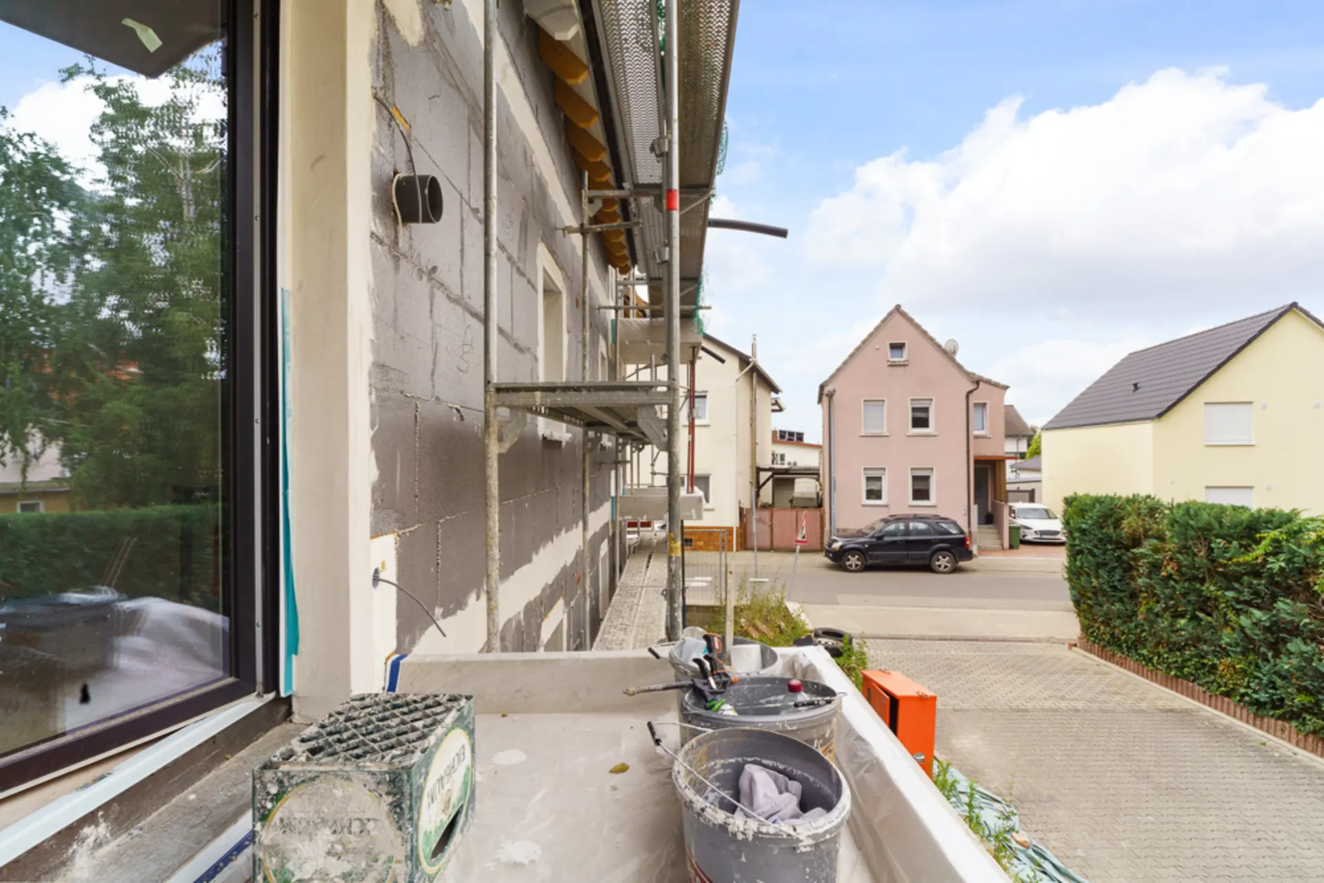 Blick von einem Balkon mit Baugerüst und Baumaterialien auf eine Wohnstraße.