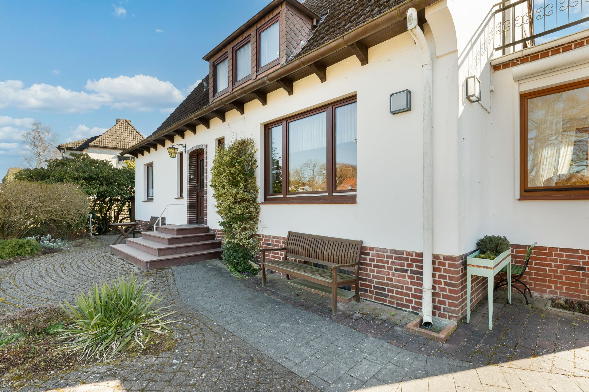 Vorderansicht eines weißen Hauses mit Bank und kleinem Tisch am Eingang.