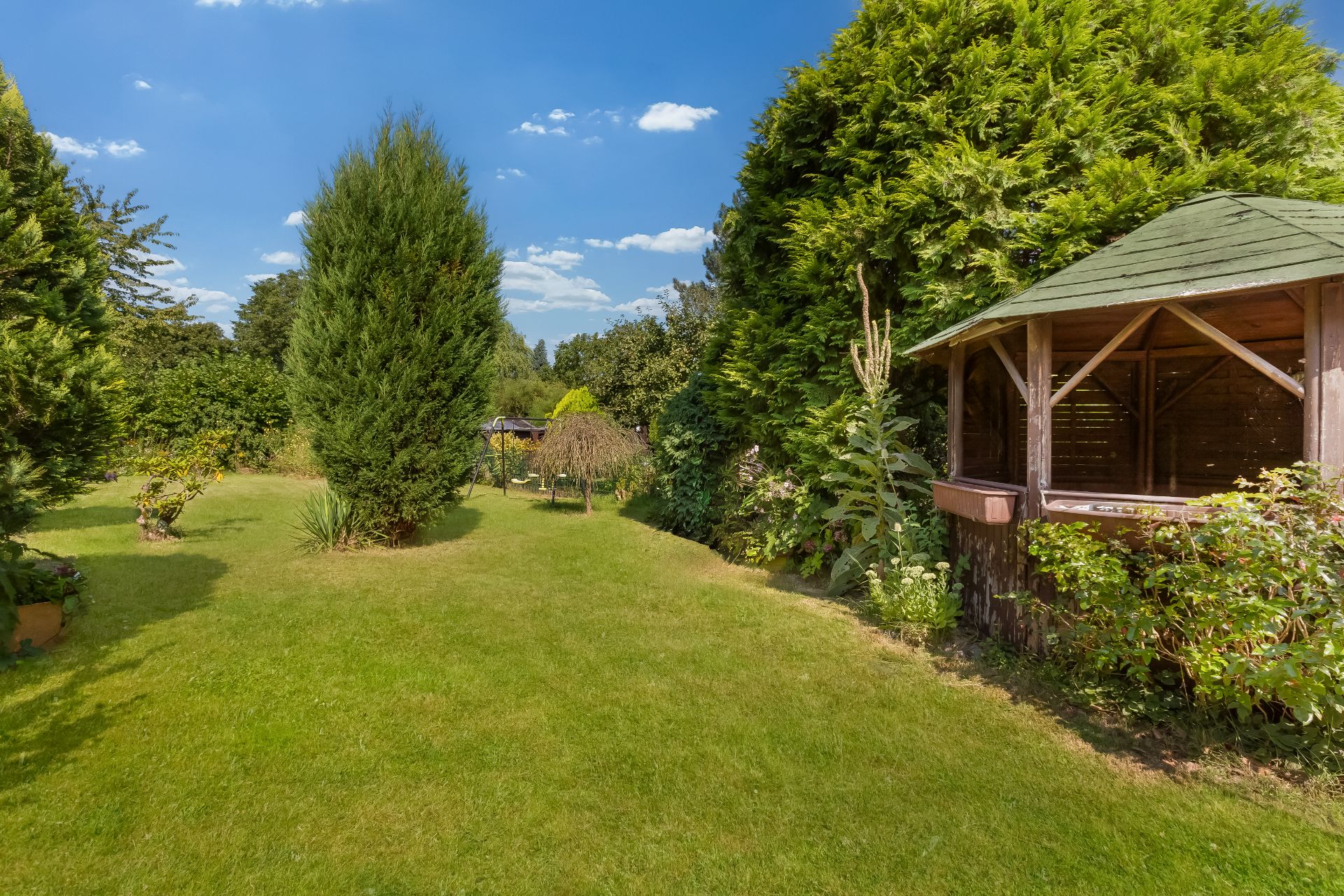 Großer Garten mit Rasenfläche, Bäumen und einer hölzernen Gartenlaube rechts.