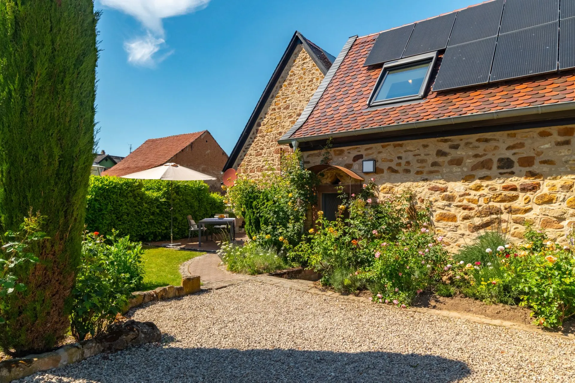 Garten mit Kiesweg, Blumenbeeten und Steinhaus mit Solarpanelen auf dem Dach.