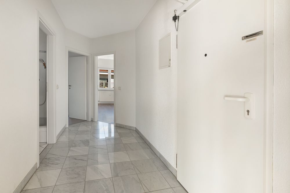 Heller Flur mit weißem Bodenfliesen, mehreren Türen und Blick in ein weiteres Zimmer.