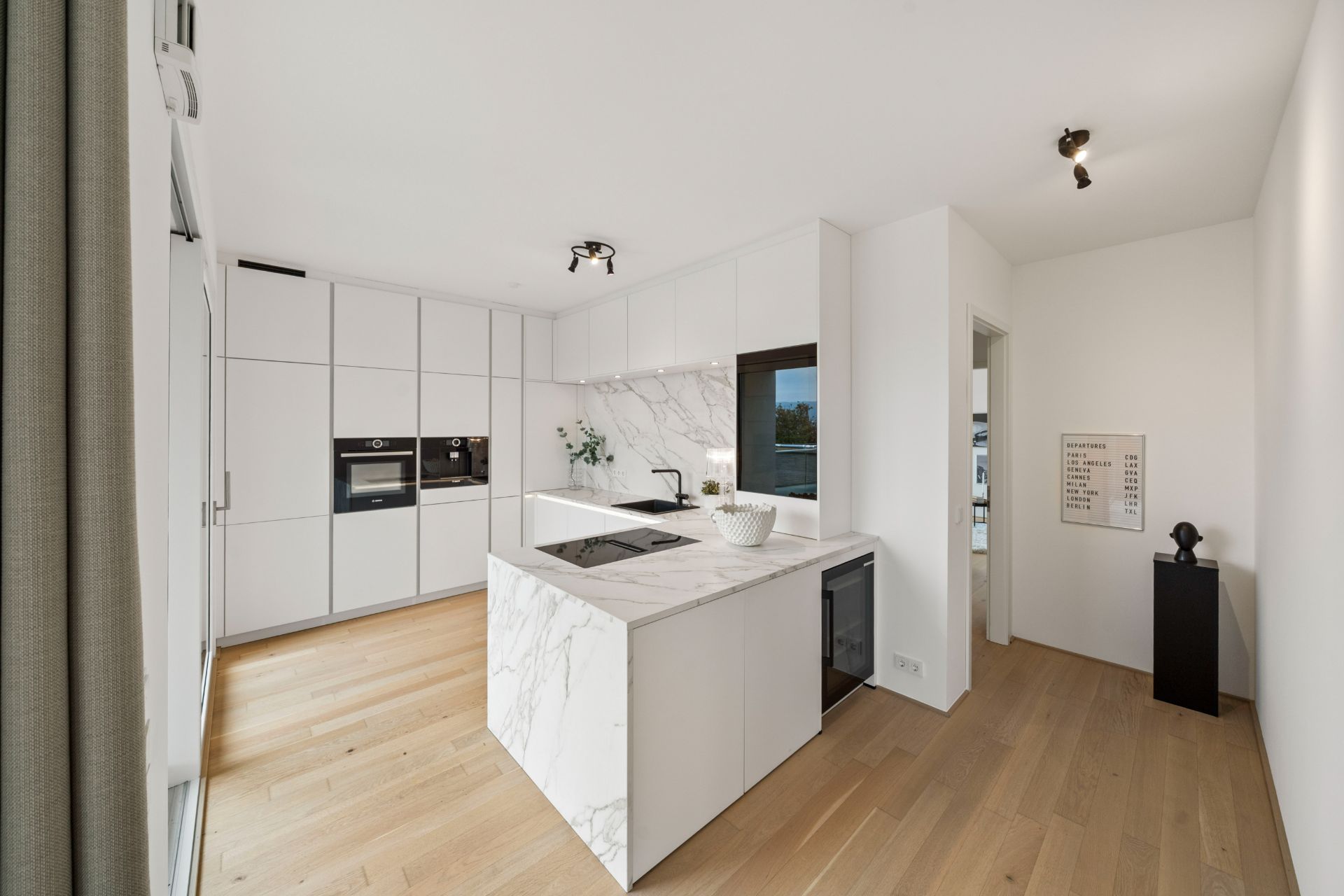 Moderne, helle Küche mit Kücheninsel, weißen Schränken und Holzfußboden.