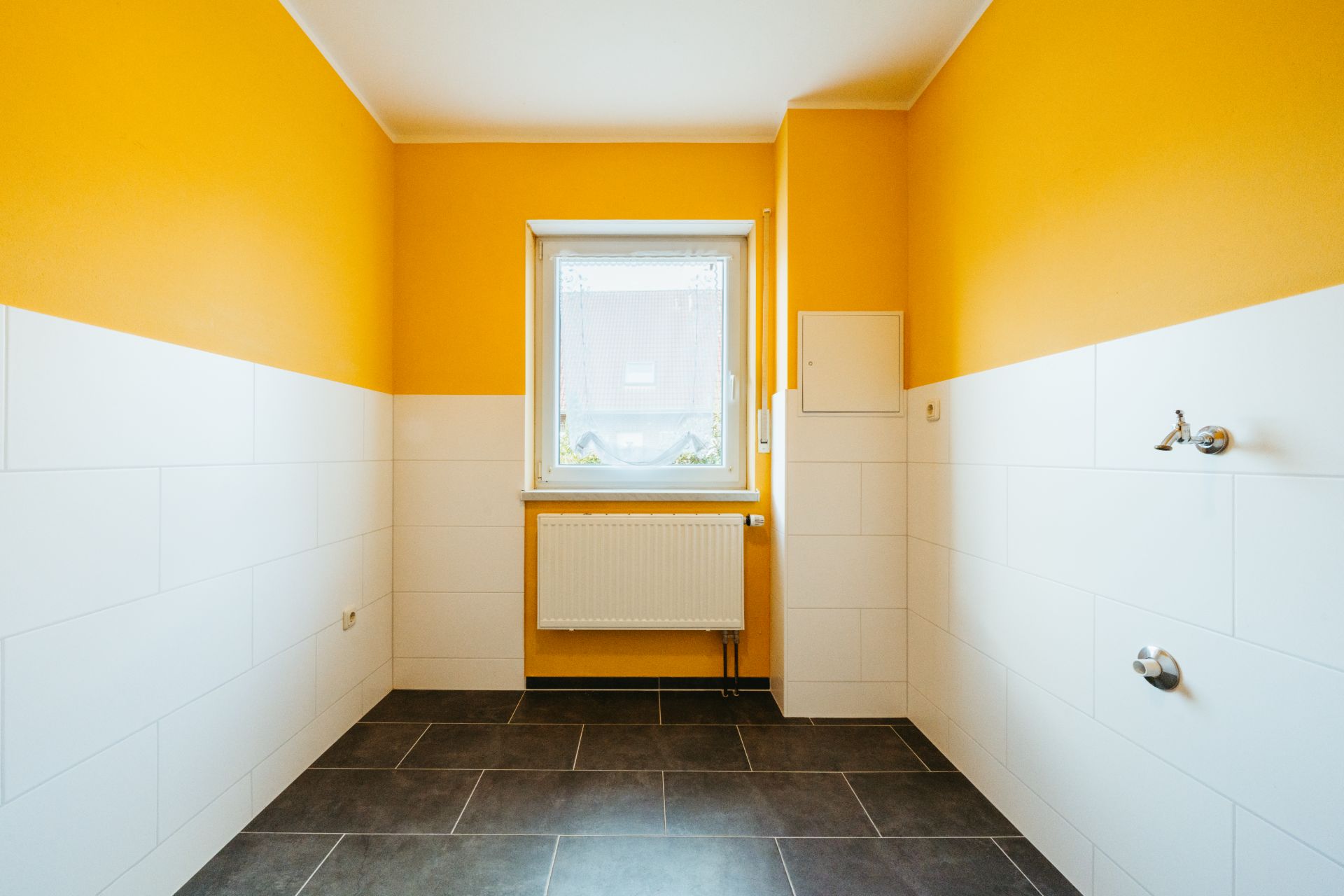 Leerer Raum mit gelben Wänden, weißem Fliesenspiegel, Fenster und Heizkörper.