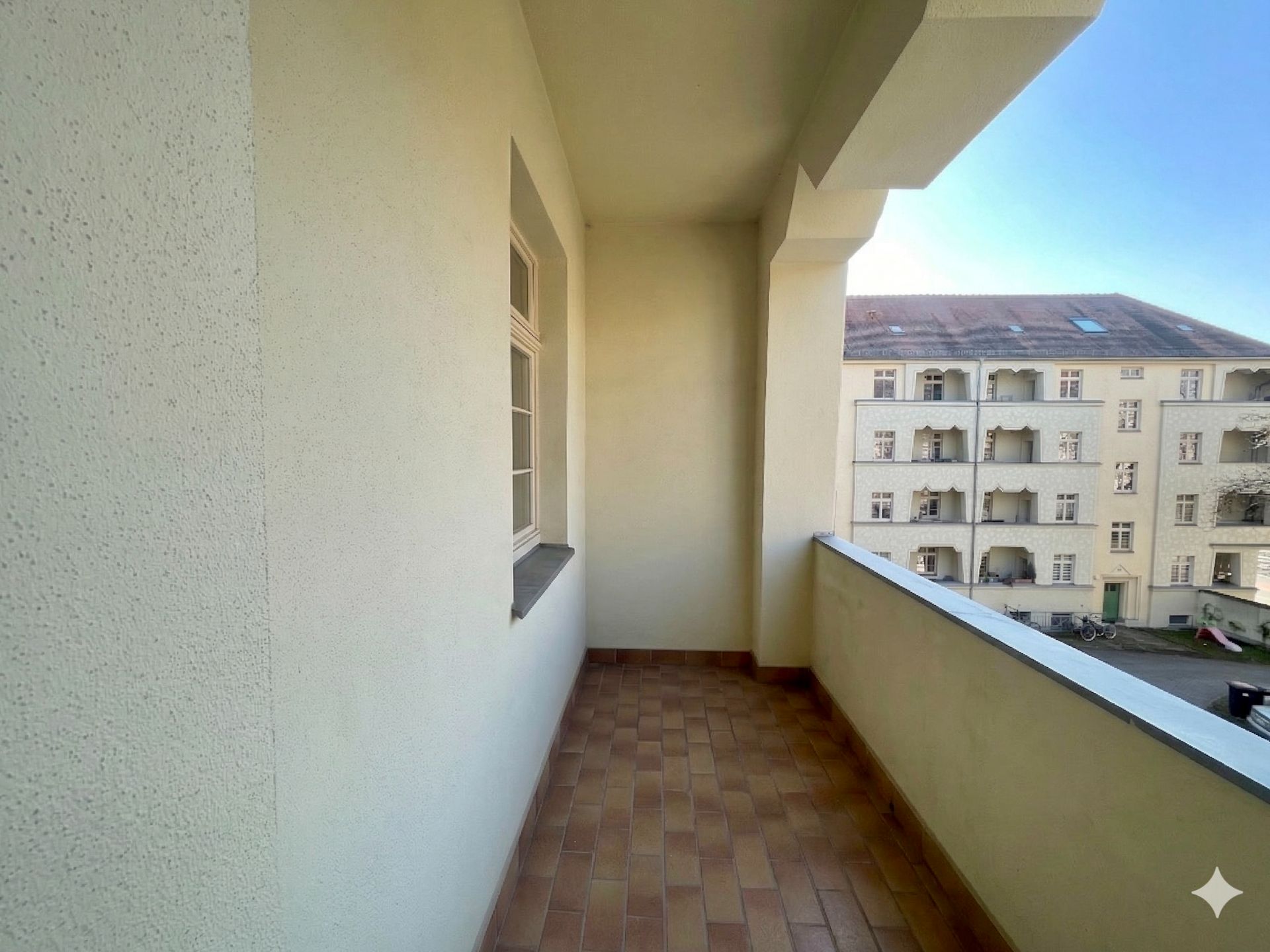 Überdachter Balkon mit Fliesenboden, Blick auf benachbarte Wohnhäuser.