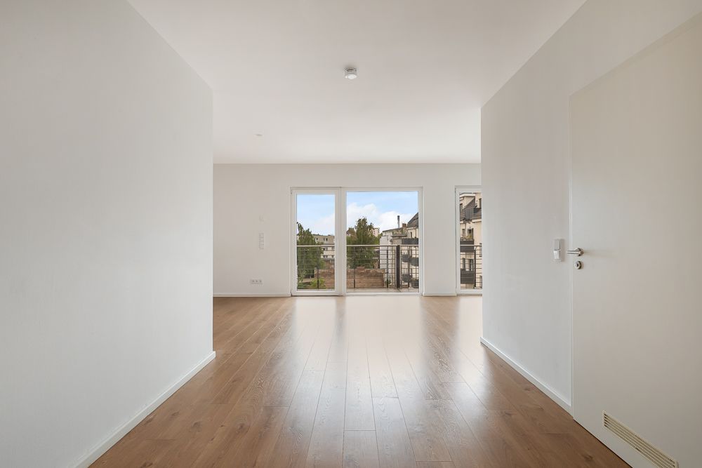 Heller Raum mit Holzboden, großen Fenstern und Blick auf einen Balkon.