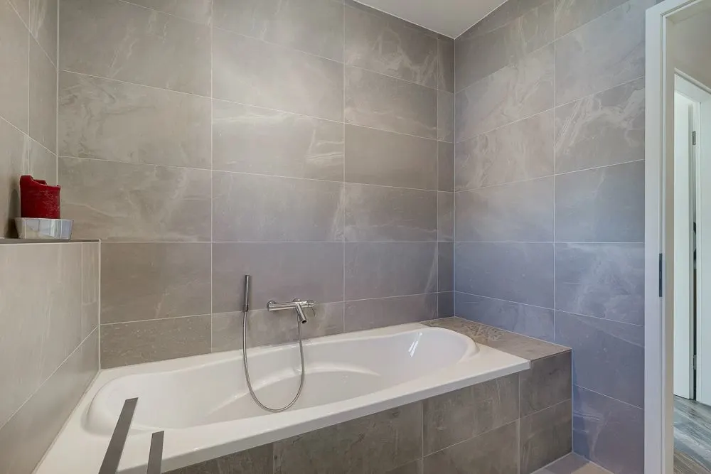 Modernes Badezimmer mit eingebauter Badewanne und grauen Wandfliesen.