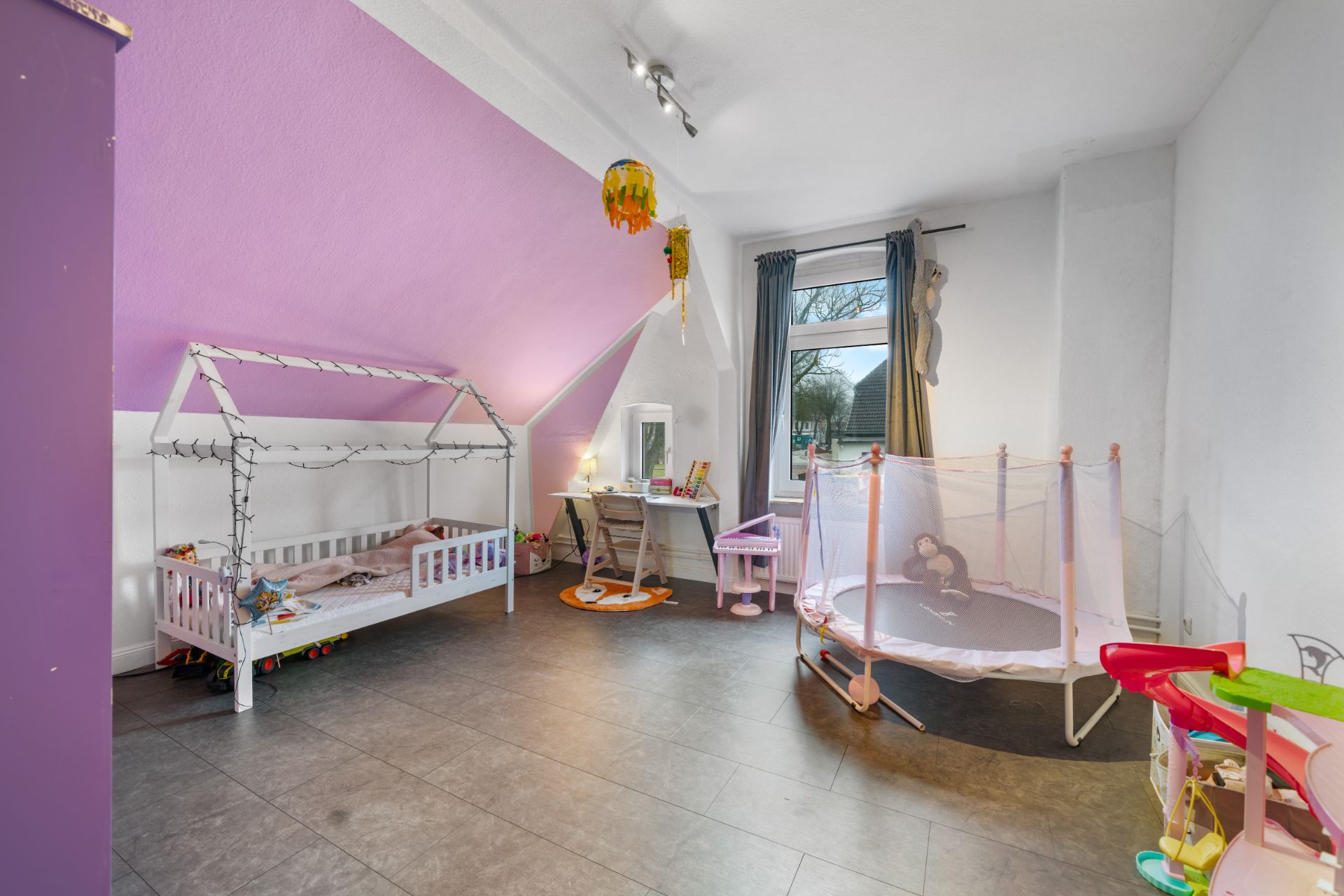 Kinderzimmer mit Hausbett, kleinem Schreibtisch, Spielzeug und lila gestrichener Wand.