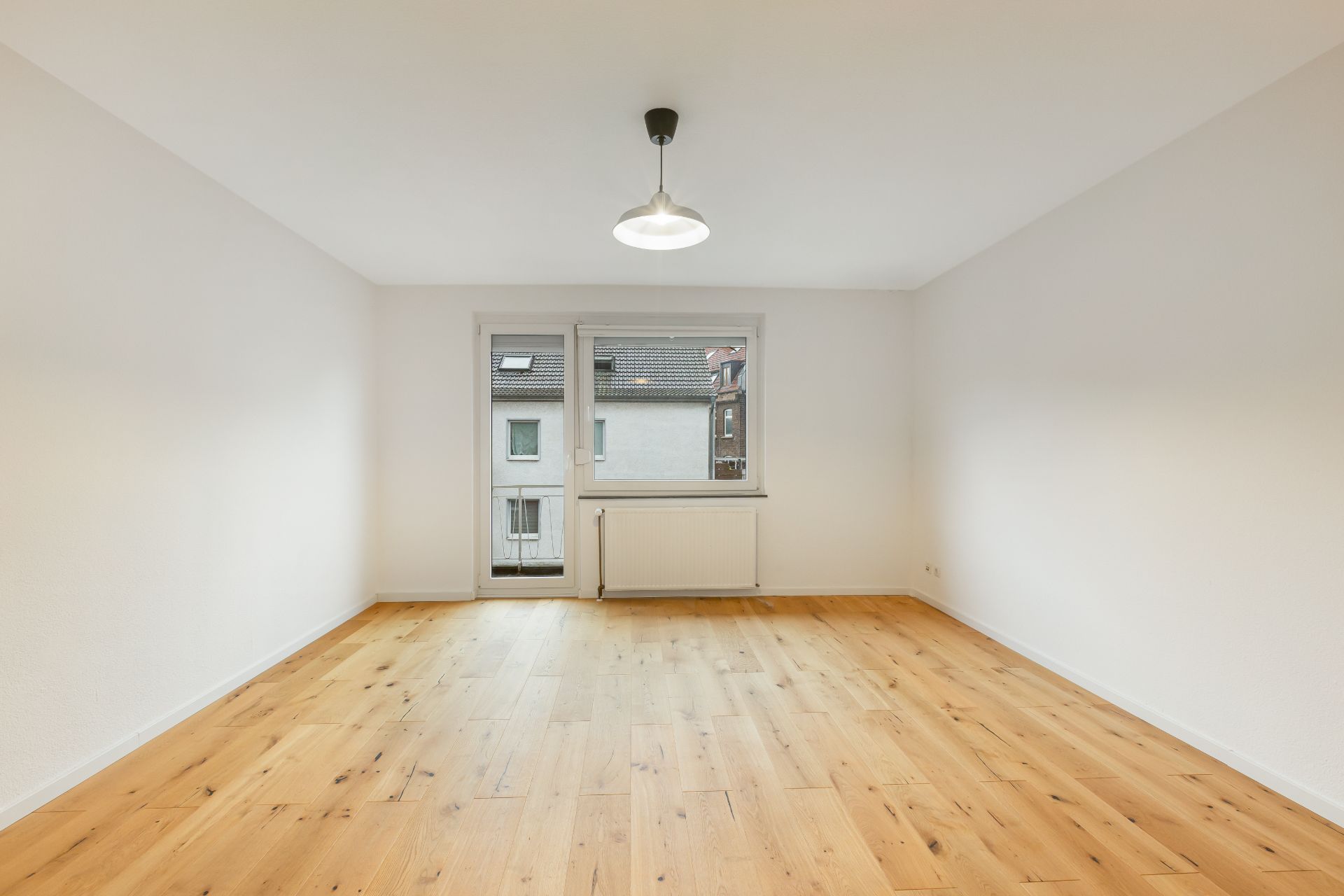 Heller, leerer Raum mit Holzfußboden, weißer Wand und Fenster mit Tür zur Außenseite.
