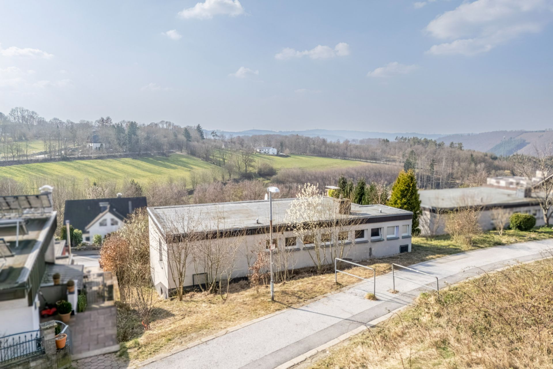 Blick auf ein flaches Gebäude mit umliegendem Grün und Hügeln im Hintergrund.