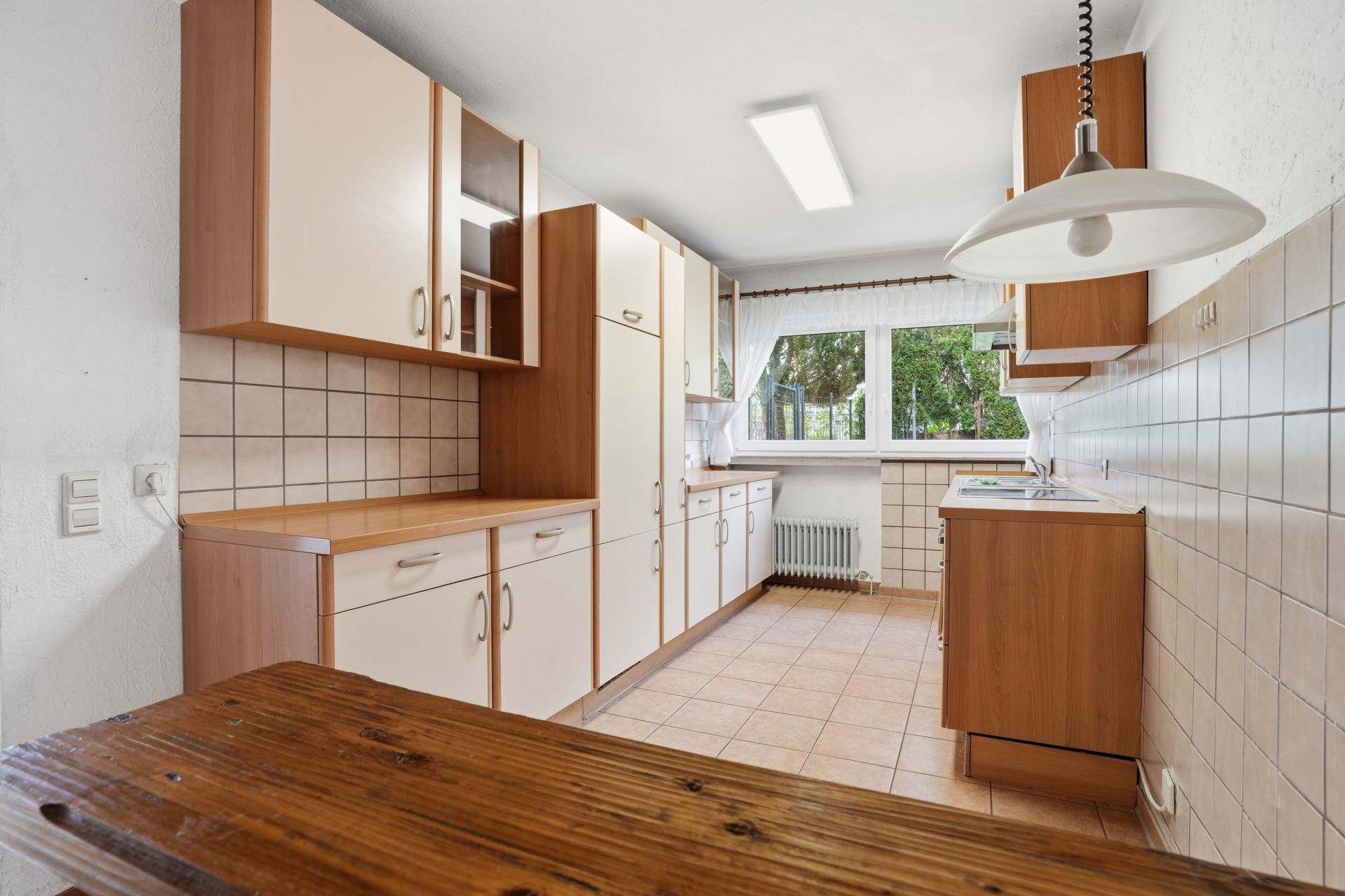 Helle Küche mit Holzschränken, Fliesenboden und großem Fenster.