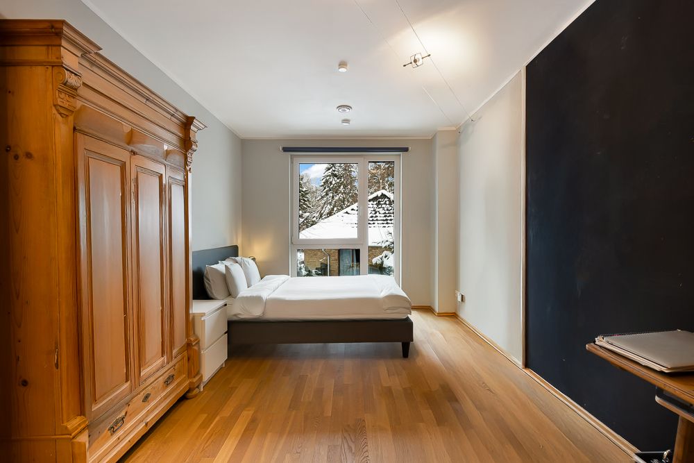 Schlafzimmer mit Holzboden, Doppelbett, großem Kleiderschrank und Fenster mit Blick auf verschneite Bäume.