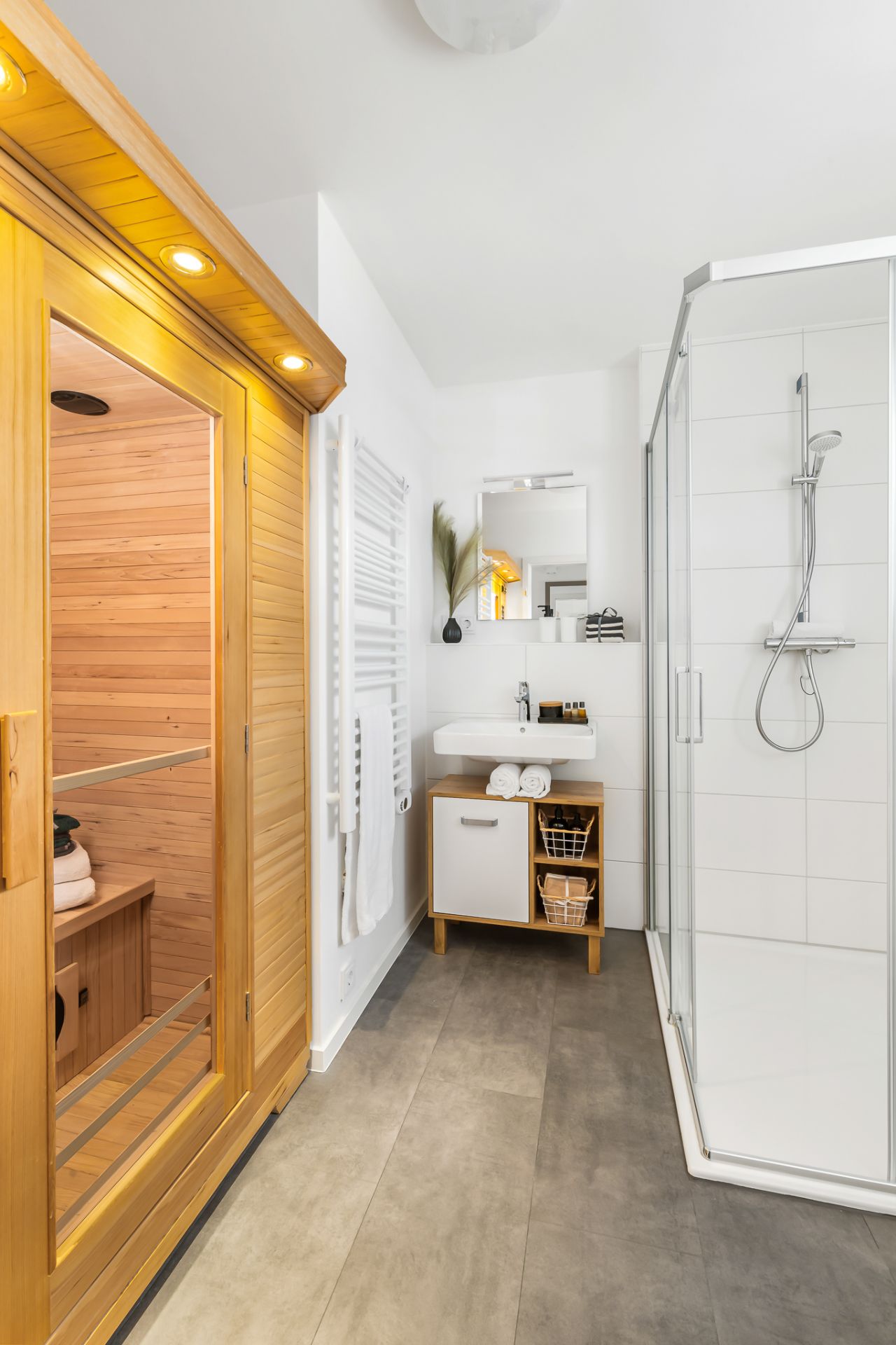 Modernes Bad mit Sauna, Dusche, Waschbecken, Spiegel und Handtuchheizkörper.