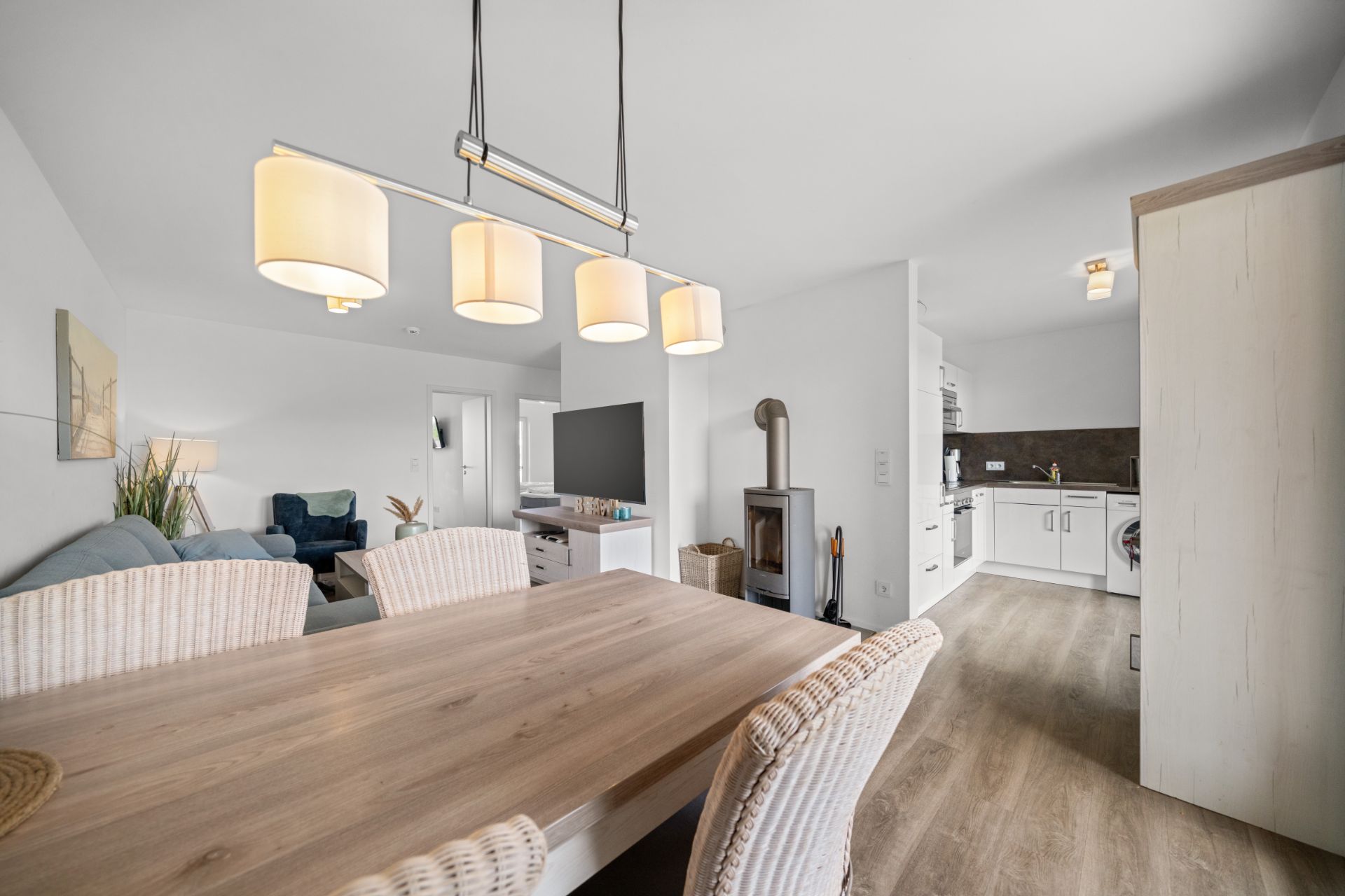Helles Wohn- und Esszimmer mit Holztisch, Kamin und offener Küche.