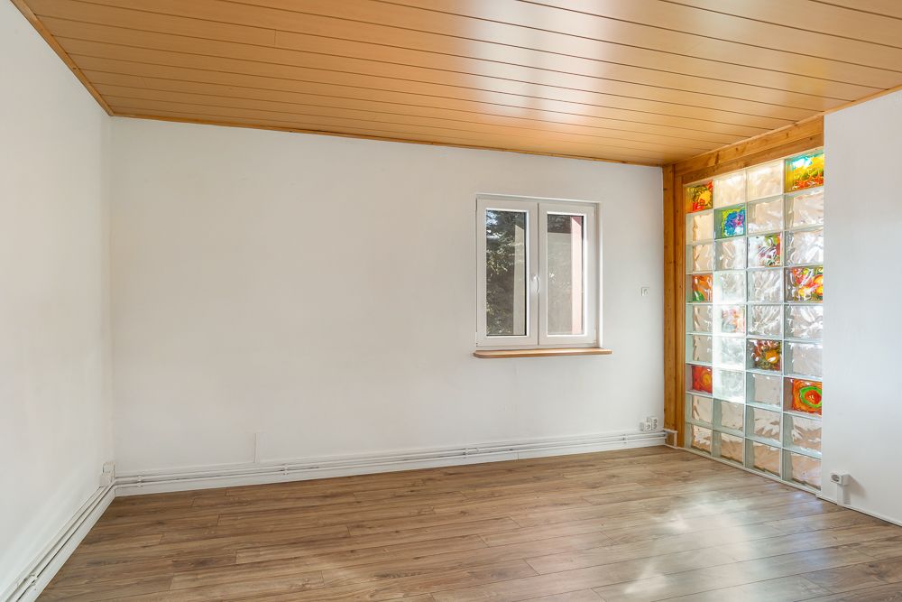 Leerer Raum mit Holzdecke, Fenster und bunter Glasbausteinwand.