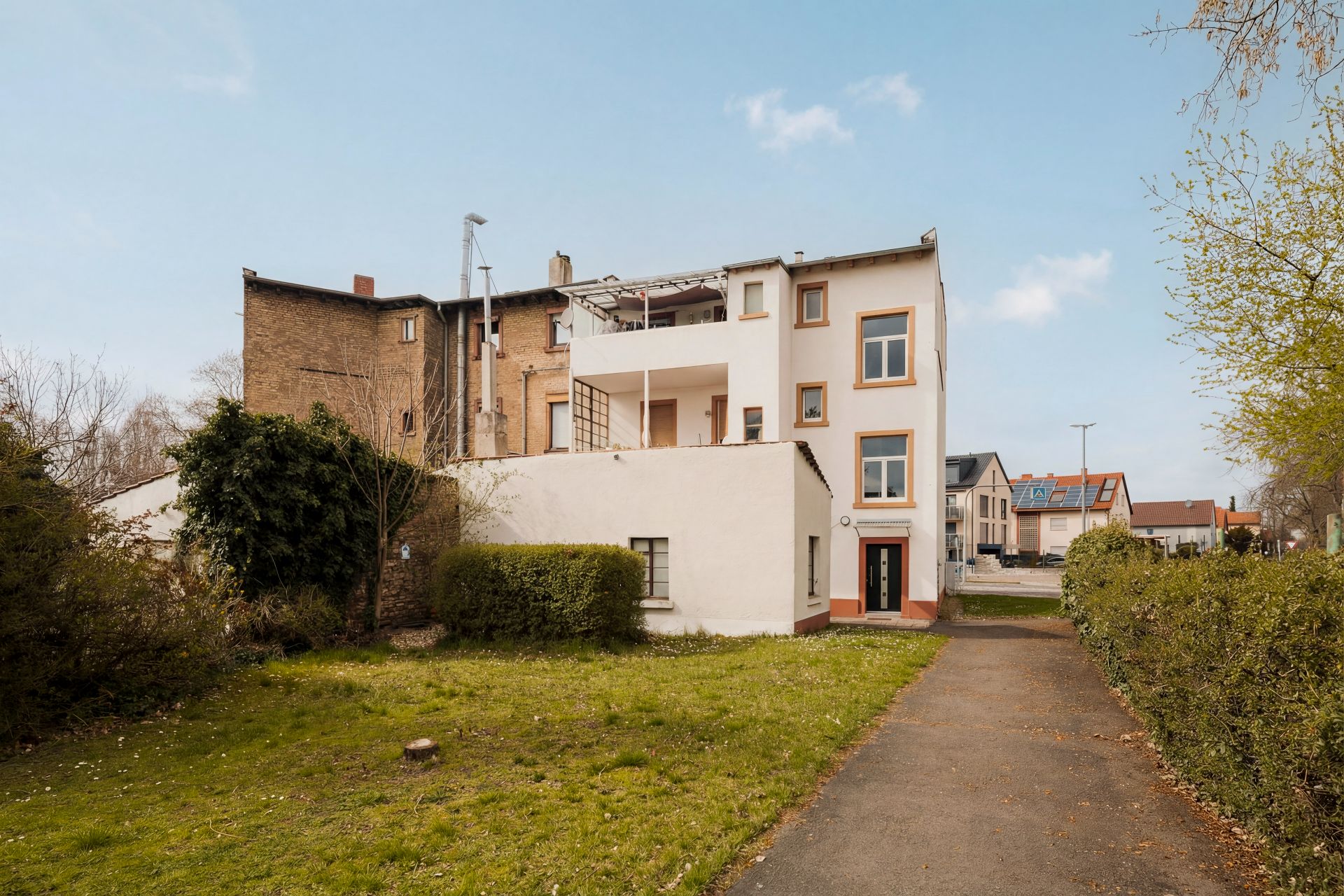 Mehrfamilienhaus mit weißer Fassade, Balkon und Vorgarten, Weg führt zum Eingang.