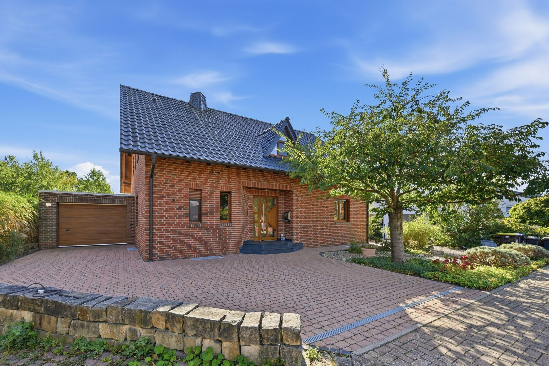 Backsteinhaus mit dunkelgrauem Dach, Einfahrt, Garage und Baum im Vorgarten.