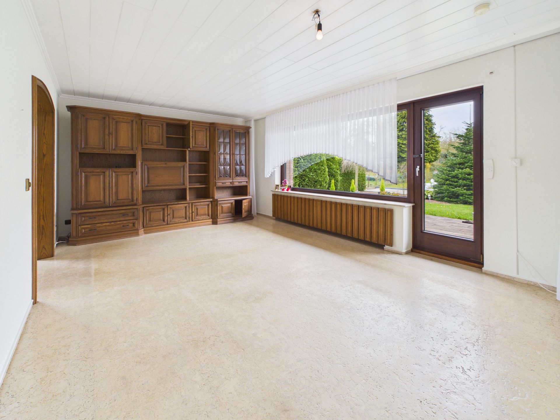 Leeres Wohnzimmer mit großem Fenster, Holztür und Einbauschrank aus Holz.