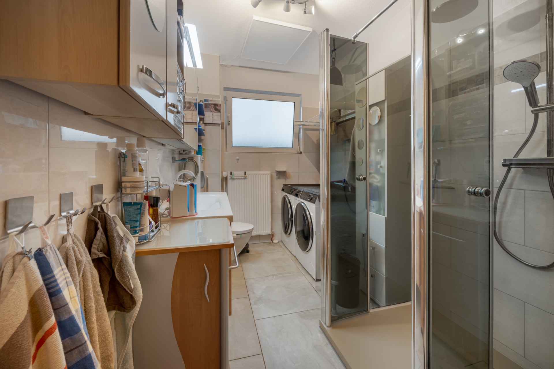 Modernes Badezimmer mit Dusche, Waschmaschine, Trockner, Waschbecken und Handtüchern.