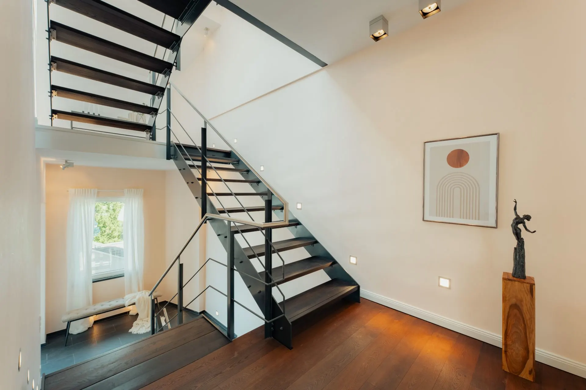 Moderne Treppe mit schwarzem Geländer, Holzfußboden, Kunstwerk und Statue auf Sockel im Flur.