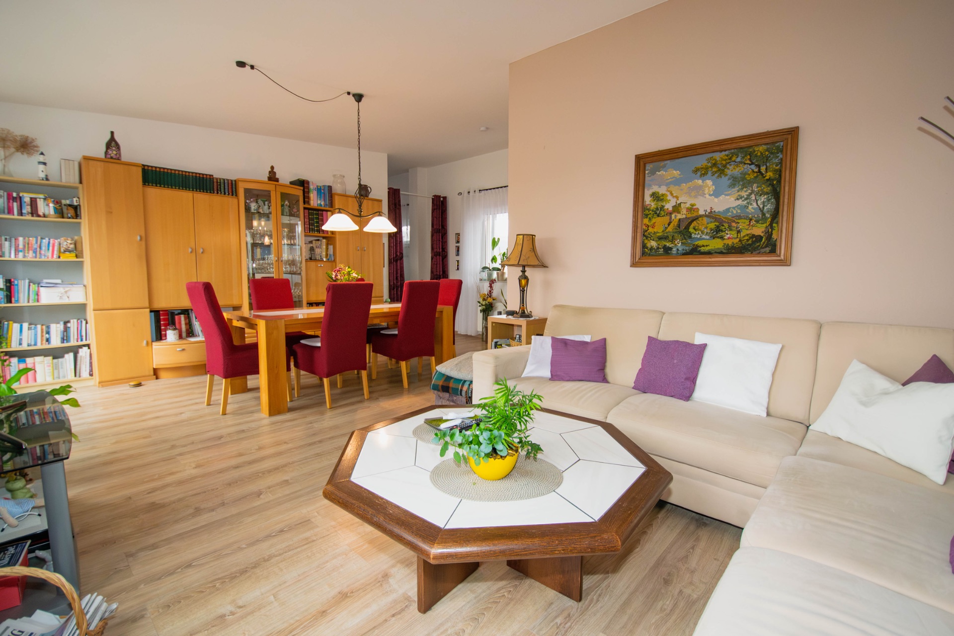 Wohnzimmer mit Ecksofa, Couchtisch, Esstisch und Bücherregal, Bild an der Wand.