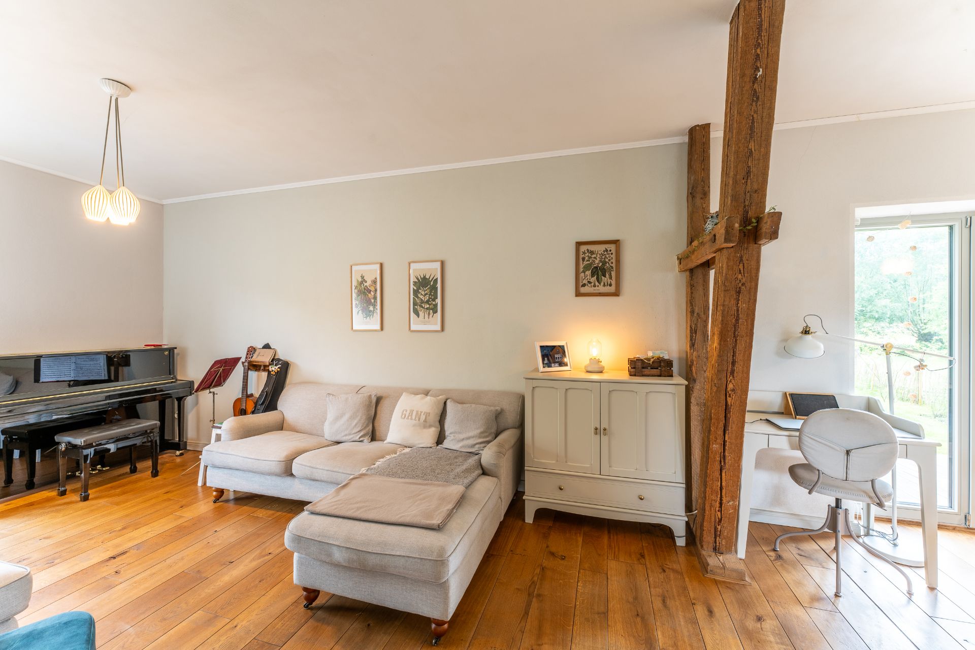 Wohnzimmer mit Sofa, Klavier, Holzfußboden, Schreibtisch und Holzbalken.