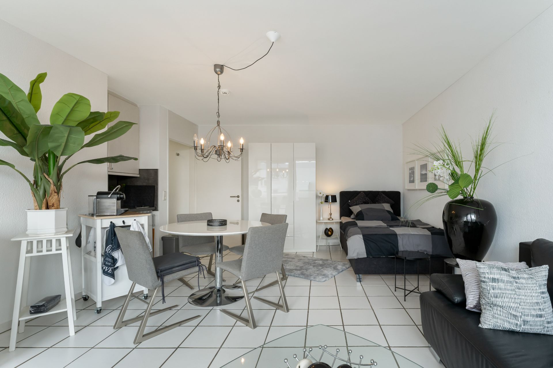 Modernes Studio mit Bett, Esstisch, Pflanzen und Sofa auf gefliestem Boden.