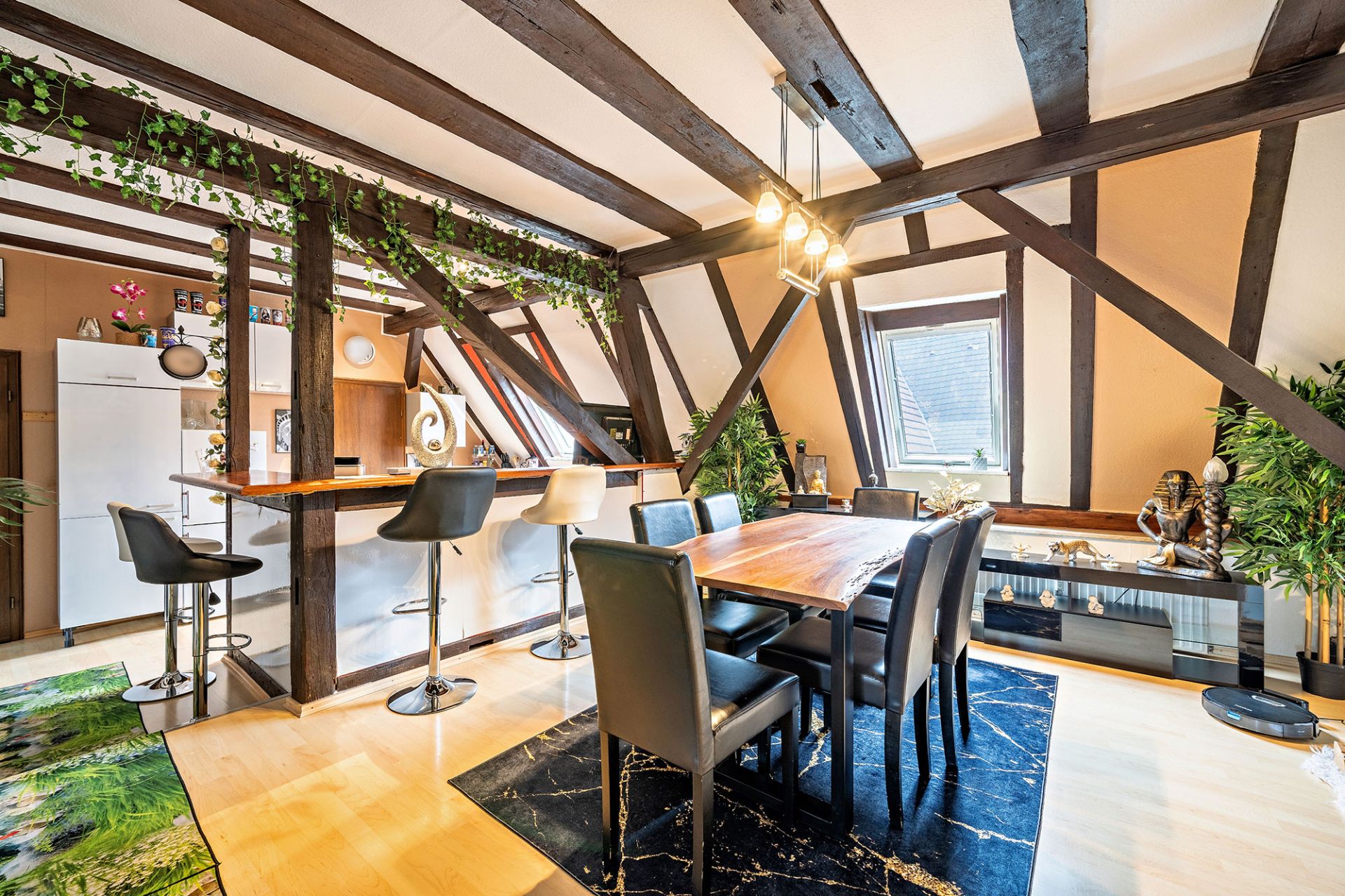 Modernes Esszimmer mit Holztisch, schwarzen Stühlen, Theke und sichtbaren Holzbalken unter dem Dach.