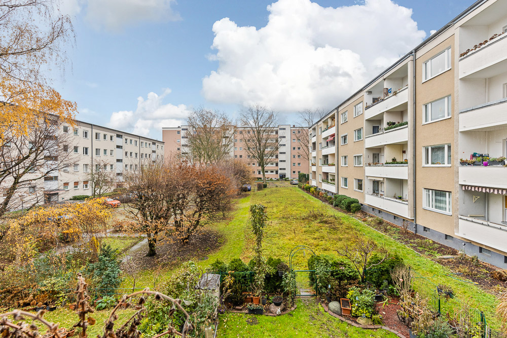 Blick auf einen begrünten Innenhof zwischen mehreren Wohngebäuden mit Balkonen.