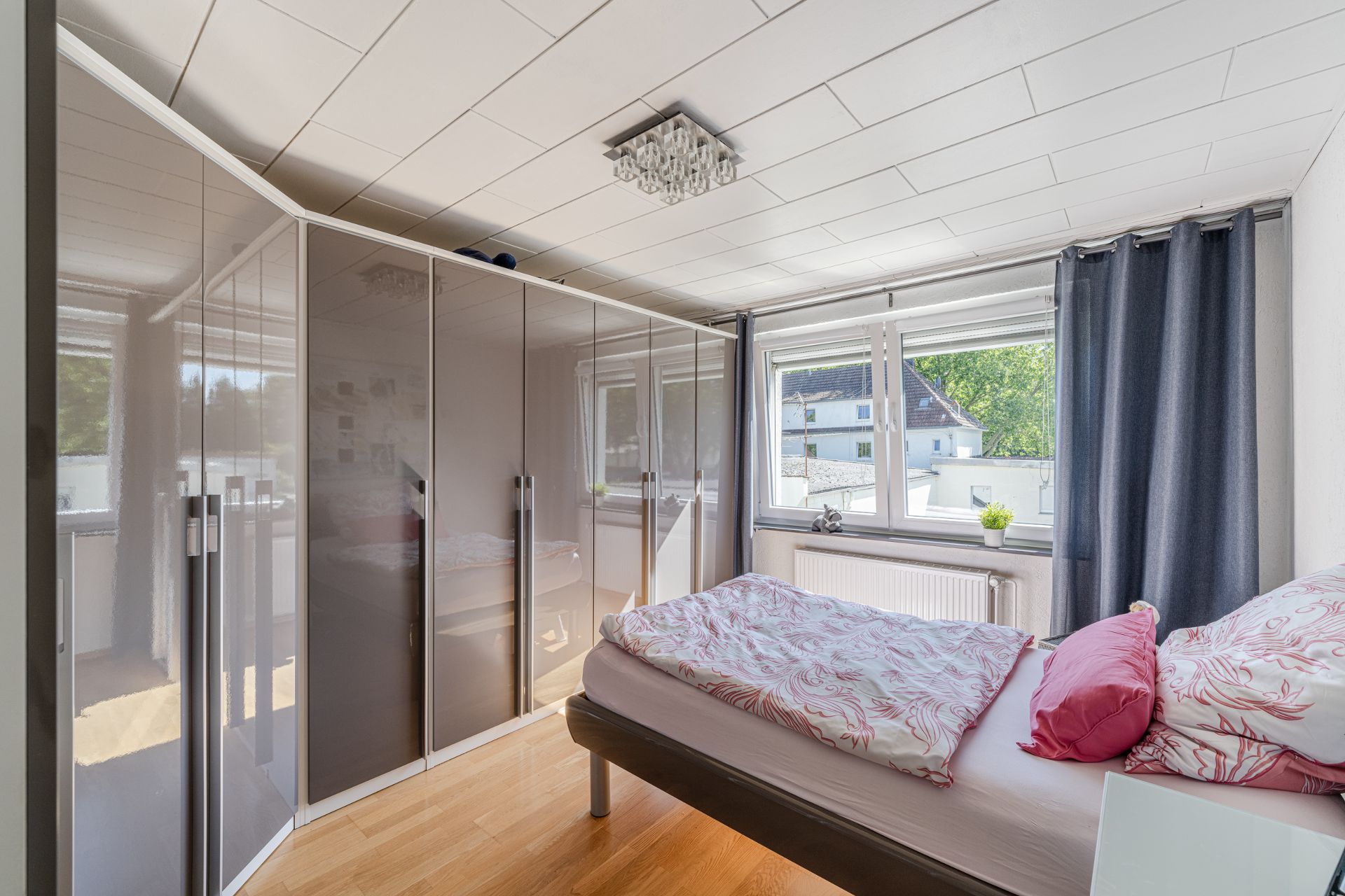 Helles Schlafzimmer mit großem Eckkleiderschrank, Bett und Fenster mit Blick nach draußen.