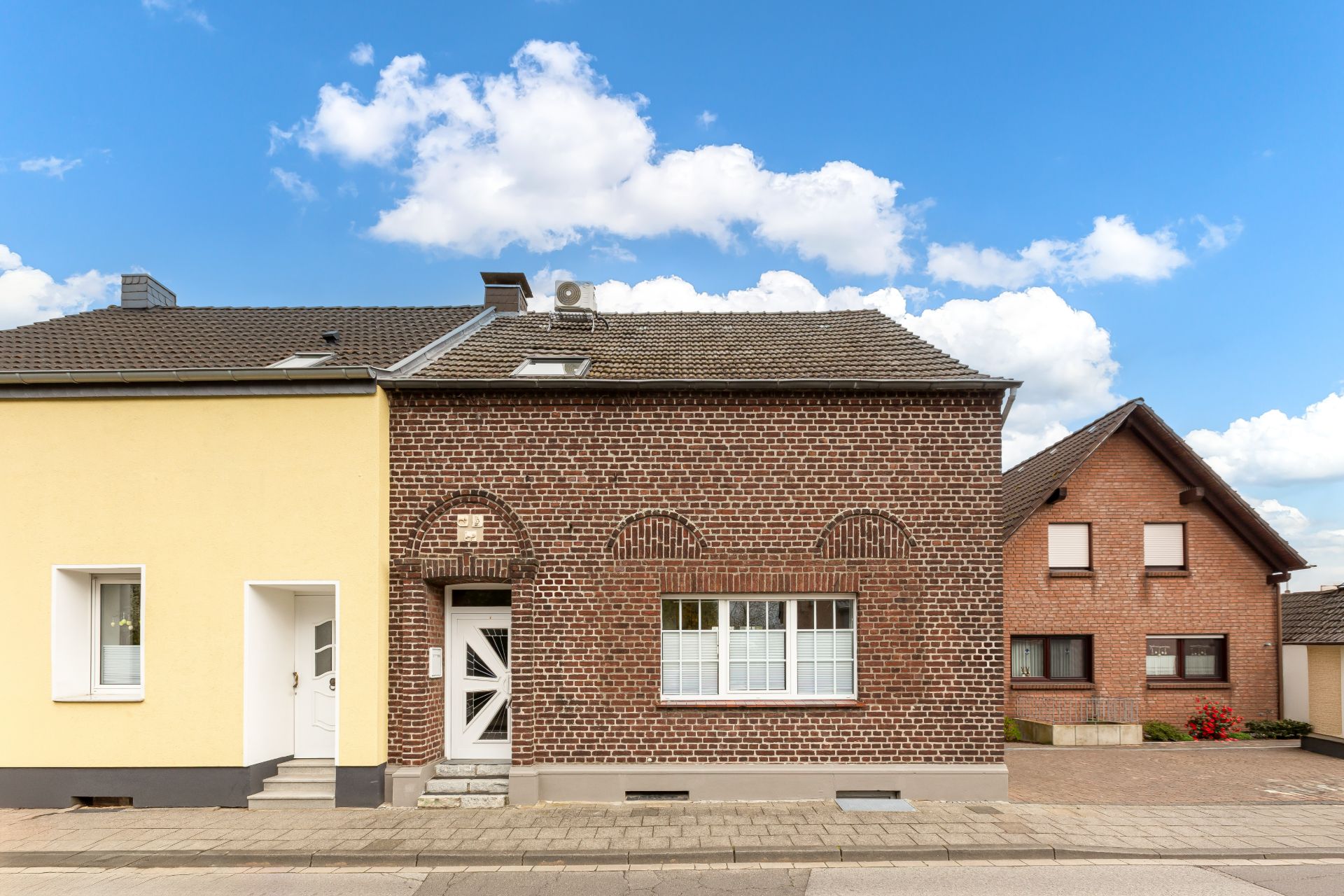 Vorderansicht eines roten Backsteinhauses mit weißer Tür und großem Fenster an einer Straße.