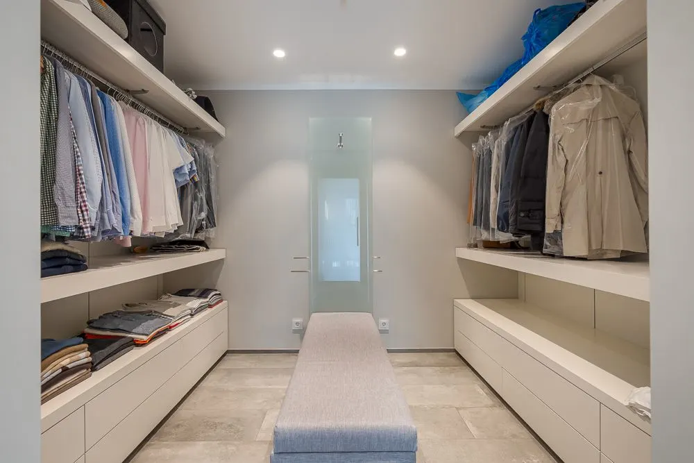 Moderner begehbarer Kleiderschrank mit Regalen, Kleidung und einer Bank in der Mitte.