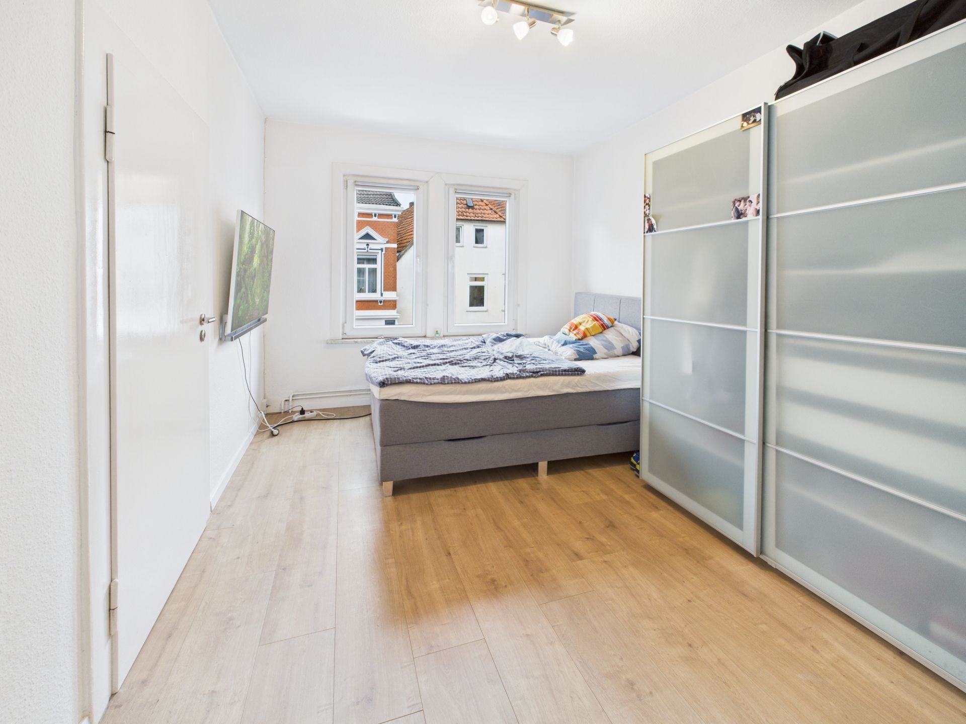 Helles Schlafzimmer mit Doppelbett, Kleiderschrank und zwei Fenstern, Holzfußboden.